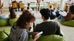 African American female student hiding while using smart phone during a casual class in campus.